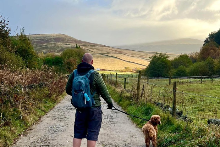 A male hiker and a dog walking up a farm track
