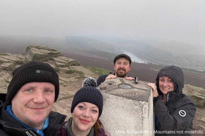 An image of two male and two female hikers at the Win Hill trig point