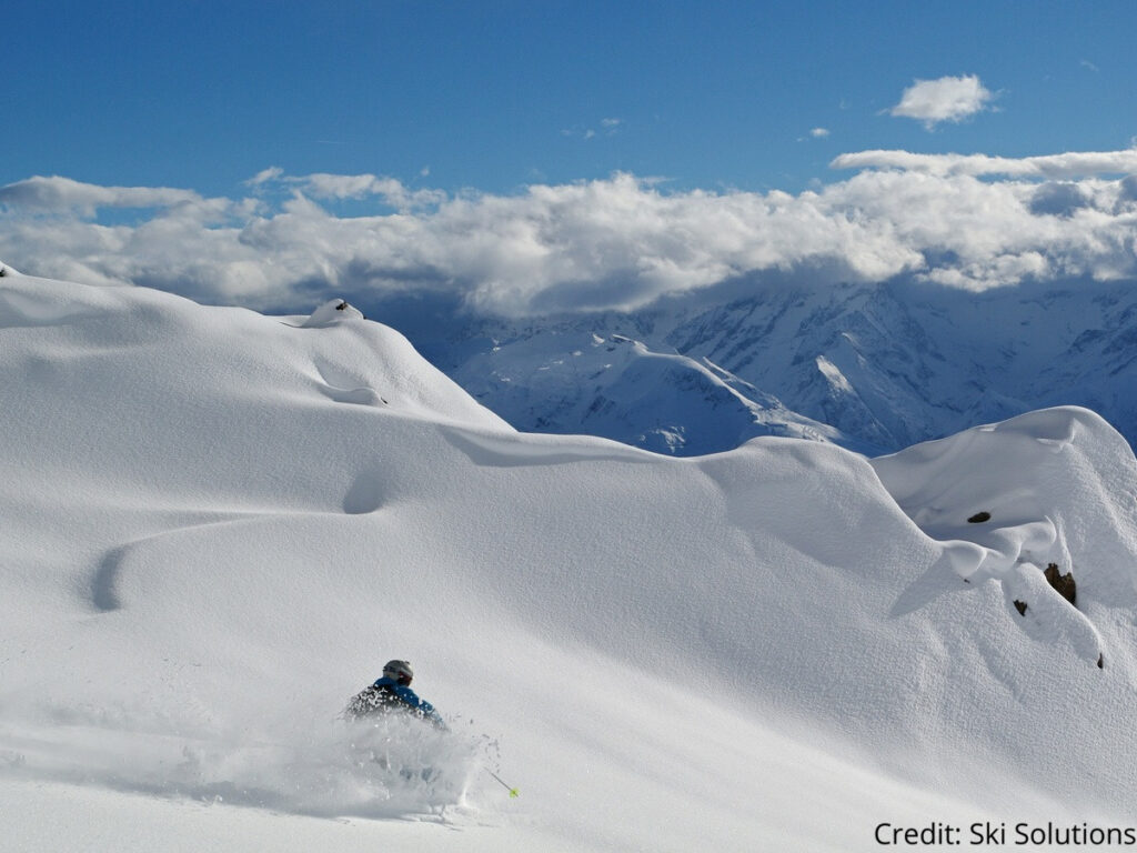 A skier coming down a route on Alpe d'Huez ski resort in sunny conditions 