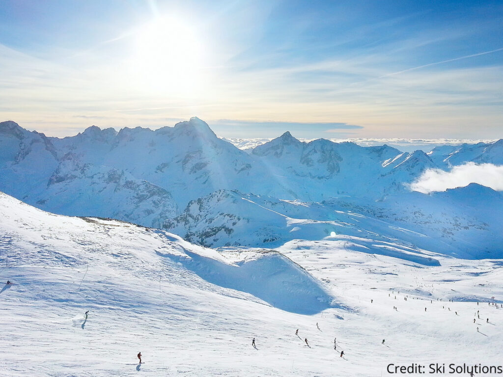 Skiers and snowboarders on a piste at Les Deux Alpes ski resort with bright blue skies