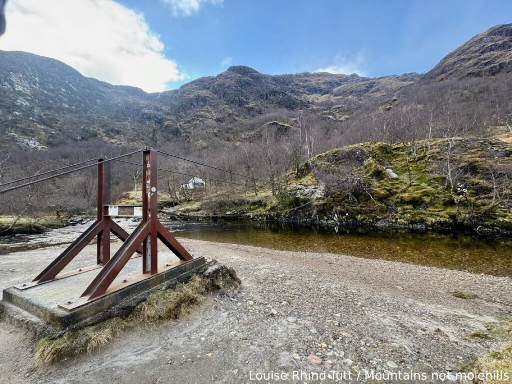 A wire bridge crossing a river with mountains in the background